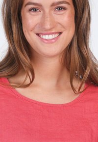 Weiches Korall-T-Shirt mit weitem Halsauschnitt, kurzen Ärmeln und glatter Textur. Das Model zeigt ein lächelndes Gesicht vor einem weißen Hintergrund.