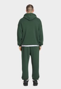 Zielona bluza z kapturem o luźnym kroju, z elastycznymi mankietami oraz dopasowanymi zwężanymi spodniami. Całość uzupełniona czarnymi trampkami i białą warstwą wewnętrzną.