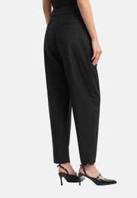 Pantaloni neri su misura con una consistenza liscia, vestibilità affusolata e tasche laterali, abbinati a décolleté nere lucide con cinturini alla caviglia.