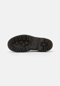 Suela de bota de goma negra con profundas estrías y un tacón redondeado. Presenta una superficie con patrón y detalles de logotipo grabados, ofreciendo tracción y durabilidad.