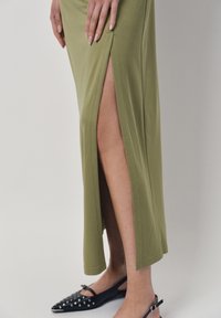Olijfgroene, aansluitende maxi-jurk met zijsplitten, gemaakt van zacht materiaal. Gepaarde met zwarte puntige ballerina's met studded accenten.