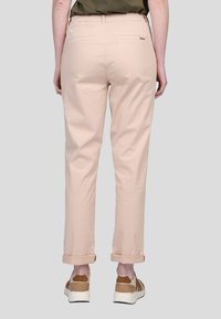 Chinos en coton rose clair à la coupe décontractée, avec des ourlets retroussés et deux poches arrière. Portés avec des baskets beiges et blanches.