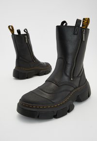 Czarne skórzane botki za kostkę z grubą gumową podeszwą, bocznym zamkiem błyskawicznym, żółtym haftem i pętelką do łatwego zakładania.