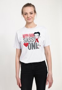 Hvid bomuld t-shirt med grafisk design, der viser teksten "BETTY BOOP SASSY" og en illustration af Betty Boop i en rød kjole.