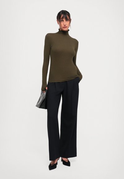 Olive green long-sleeve turtleneck top paired with high-waisted black wide-leg trousers and black pointed-toe heels, holding a black clutch.