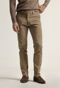 Chinos de algodón color beige con un corte recto, que cuentan con un cierre de botón frontal, bolsillos laterales y una textura suave. Unos zapatos marrones complementan el conjunto.