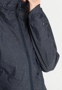 Ciemnoszara, lekka kurtka z teksturowanej tkaniny, z zamkiem błyskawicznym z przodu i kapturem. Posiada subtelny wzór w paski oraz elastyczne mankiety.