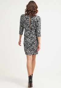 Svart och vitt mönstrad klänning med trekvartslånga ärmar, figursydd design, synlig slits i ryggen, och bärs med svarta ankelkängor.