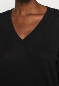 Czarny sweter z dzianiny z dekoltem w serek i prążkowanymi wykończeniami, o miękkiej fakturze i prostych liniach. Materiał wydaje się lekki i dopasowany do sylwetki.