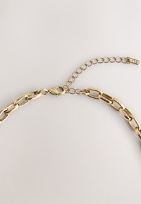 Gold chain necklace with large links, finished with a lobster clasp and an adjustable chain. Polished surface with minimal texture.