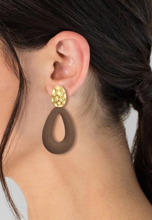Los pendientes en tono dorado cuentan con una parte superior circular texturizada y un diseño de gota marrón curvado, destacando líneas suaves y un centro abierto.
