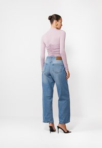 Fioletowa bluzka z długim rękawem i marszczonym tyłem, zestawiona z niebieskimi spodniami dżinsowymi o wysokim stanie i czarnymi szpilkami. Minimalistyczny design.