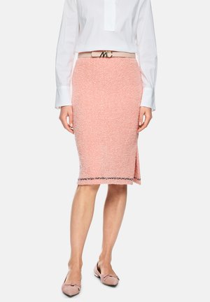 Woman wearing a pink textured knee-length skirt with a side slit, beige belt with gold buckle, white long-sleeve shirt, and pink flats.