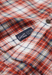 Camicia di flanella a quadri rossi e blu, con colletto abbottonato e un'etichetta con scritto "Superdry", realizzata in un tessuto morbido e dal motivo a trama.
