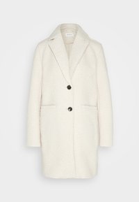 Abrigo blanco texturizado con solapa de muesca, dos bolsillos frontales y cierre de doble botón. Presenta un corte relajado y una tela suave.