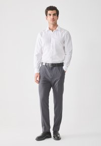 Witte overhemd met knopen, grijze broek, zwarte leren riem en zwarte schoenen. Minimalistisch ontwerp, gladde stof, aansluitende pasvorm.