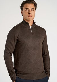 Pullover castanho com fecho na gola em material de malha suave, com mangas longas e bainha canelada. Design simples e clássico com textura subtil.