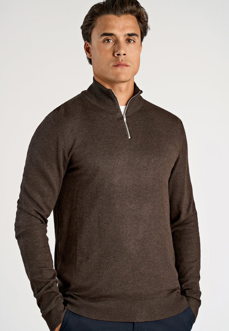 Pullover castanho com fecho na gola em material de malha suave, com mangas longas e bainha canelada. Design simples e clássico com textura subtil.