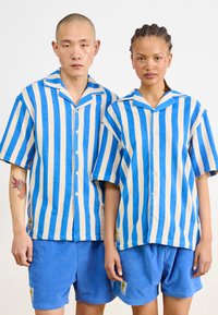 Ontspannen pasvorm, hemden met korte mouwen in blauw en beige verticale strepen, gecombineerd met effen blauwe shorts. Textuurstof met knopen aan de voorkant.