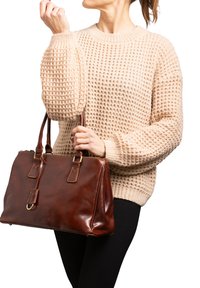 Borsa a tracolla in pelle marrone con dettagli dorati, forma rettangolare, dotata di doppi manici e chiusura con cerniera. Indossata con un maglione beige testurizzato.
