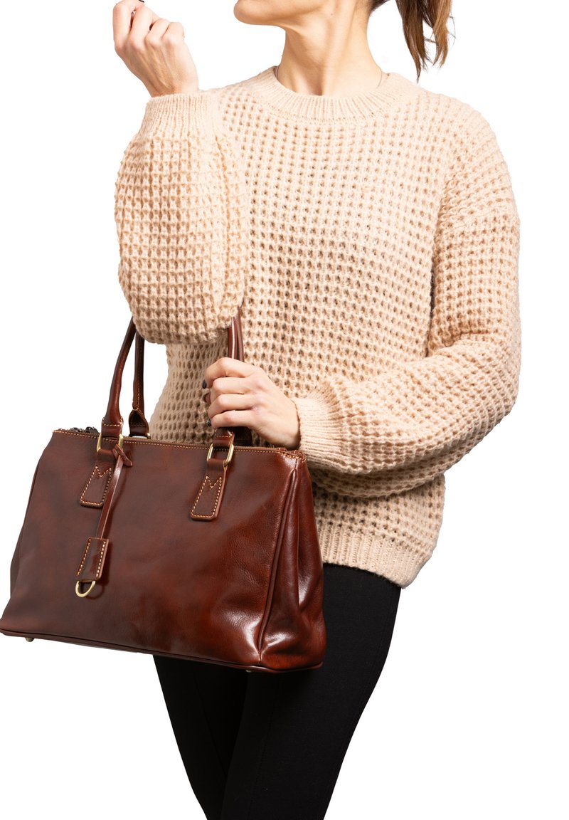 Borsa a tracolla in pelle marrone con dettagli dorati, forma rettangolare, dotata di doppi manici e chiusura con cerniera. Indossata con un maglione beige testurizzato.