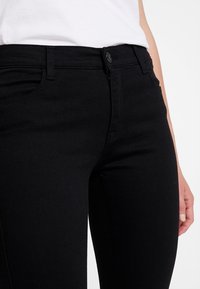 Jeans de mezclilla negros con un ajuste slim, que cuentan con cremallera, bolsillos frontales y costuras en contraste. La tela es suave y con un ligero estiramiento.