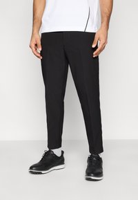 Μαύρο παντελόνι κομμένο στα μέτρα με στενή εφαρμογή, λεία υφή και πλαϊνές τσέπες, σε συνδυασμό με μαύρα παπούτσια με κορδόνια και γκρι κάλτσες.