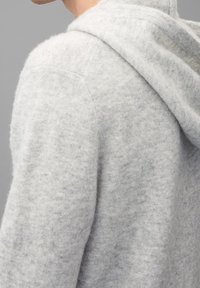 Grauer Hoodie aus einem weichen, strukturierten Stoff. Bietet einen lockeren Schnitt mit einer Kapuze mit Kordelzug und sichtbaren Nahtdetails an den Schultern.