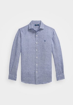 Mėlynos ir baltos langeline raštuotos ilgomis rankovėmis marškiniai su mygtukų užsegimu, turi mažą siuvinėtą logotipą kairėje krūtinės pusėje ir baltus mygtukus.