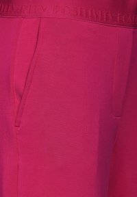 Fuchsia sportieve broek met een zachte textuur, elastische tailleband met "POSITIVITEIT" geperst, en zijzakken.