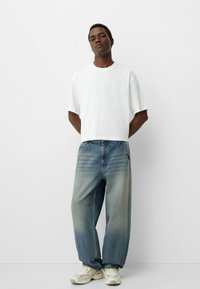 White cropped t-shirt, loose faded blue jeans, and light gray sneakers. Smooth texture with simple design, standing against a plain backdrop.