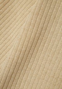 Beige ribbad tyg med fina glittrande accenter, som visar en texturerad yta och vertikala linjer. Mjukt och lätt material.