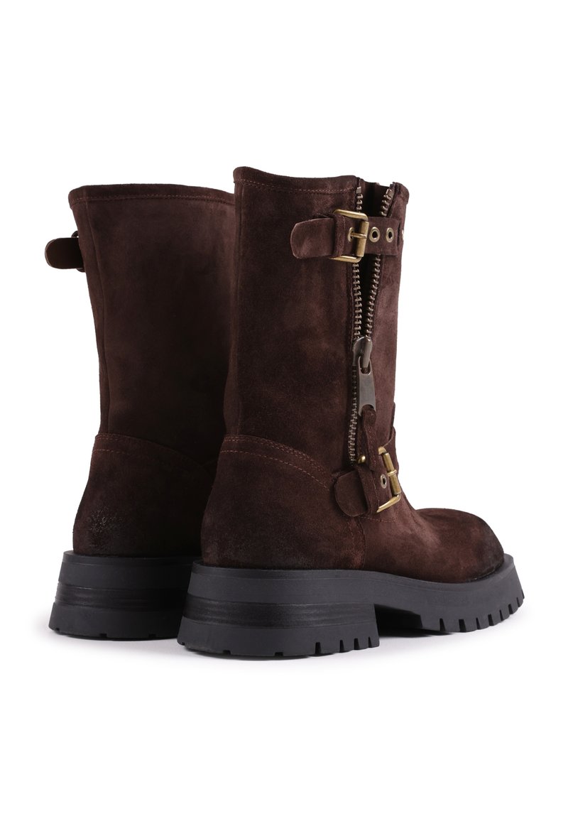 Braune Wildleder-Stiefel in Knöchelhöhe mit einem seitlichen Reißverschluss, goldfarbenen Metallakzenten und einer schwarzen Gummisohle mit einem Profilmuster.