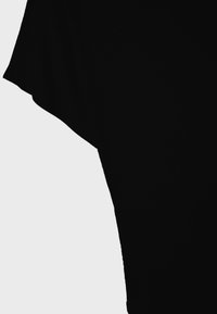 Gros plan sur une manchette de chemise noire à manches courtes sur un fond gris clair, mettant en valeur la texture du tissu et la forme.