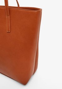 Brown leather tote bag with a textured finish, structured shape, and flat handles. Features a minimalist design and open top for easy access.