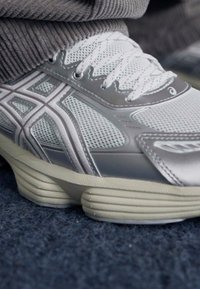 Light gray athletic shoe with mesh and synthetic overlays, featuring a thick sole and white laces, detailed with subtle accents.