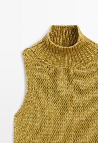 Maglione smanicato a dolcevita in una tonalità dorata. Presenta un colletto alto a coste e una superficie texture. Il tessuto ha un aspetto morbido e caldo.