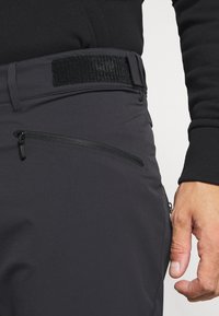 Čierne vonkajšie nohavice majú slim fit strih, textúrovaný pás, bočnú vrecko so zipsom a hladkú tkaninu pre funkčnosť a pohodlie.