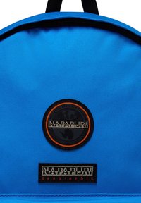 Zaino blu realizzato in tessuto texturizzato, con un logo rotondo nero e arancione e un'etichetta nera con testo bianco nella parte inferiore.