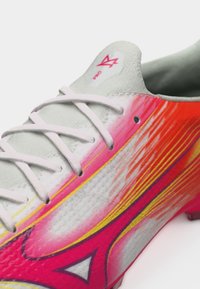 Άσπρο παπούτσι με ροζ, κόκκινα και κίτρινα σχέδια που μοιάζουν με φλόγες και λευκά κορδόνια, δείχνοντας μέρος της γλώσσας με κόκκινο λογότυπο και το κείμενο "PRO".