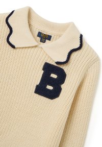 Pull en tricot couleur crème avec un col en forme de feston bleu marine et une application en feutre bleu marine en forme de "B" sur le devant. Les étiquettes indiquent la marque OVS Kids.