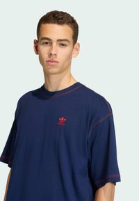 Námořnická modrá oversized tričko s červenými akcenty a prošíváním. Obsahuje malé červené logo na oblasti hrudníku. Měkká tkanina, uvolněný střih.