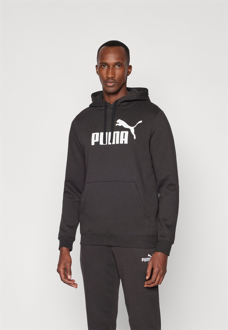 Schwarzer Hoodie aus weichem Stoff mit Kängurutasche, Kapuze mit Kordelzug und weißem Branding. Kombiniert mit passenden Sweatpants.