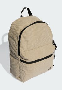 Beige, textúrájú hátizsák lekerekített tetejével, fekete cipzárral és elülső zsebbel. Jellemzője a felső fogantyú és állítható pántok.