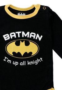 Black long-sleeve onesie with yellow neckline and accents, featuring "BATMAN" text and a yellow bat logo, cotton material, snaps at shoulder.