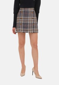 Jupe mini à carreaux en marine, blanc et marron avec un tissu texturé, dotée de boutons croisés et d'un ourlet effiloché.