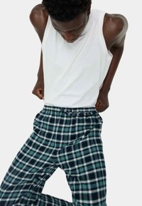 Geruite pyjamabroek in groen, marineblauw en wit, met een strikceintuur en een losse pasvorm, gecombineerd met een mouwloos wit tanktop.