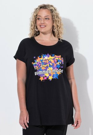 Femme aux cheveux blonds bouclés portant un T-shirt noir avec des étoiles colorées et le texte "Rock On Summer Moos", souriante et regardant sur le côté.