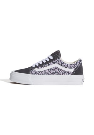 Zapatilla deportiva baja en blanco y negro con cordones blancos y patrón floral en los paneles laterales y el talón sobre un fondo blanco.