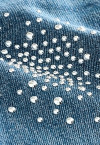 Denimtyg i en ljusblå nyans med metalliska silverpärlor i olika storlekar som är arrangerade i ett spritt mönster över ytan.